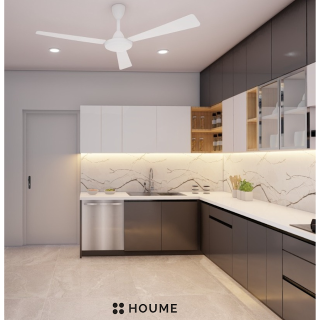 Modern kitchen with black stainless steel stovetop, oven, and vent hood, light wood cabinets, and a white quartz countertop. A ceiling fan with woven blades hangs from the ceiling. Text overlay: Houme India - Kitchen Design Ideas. B