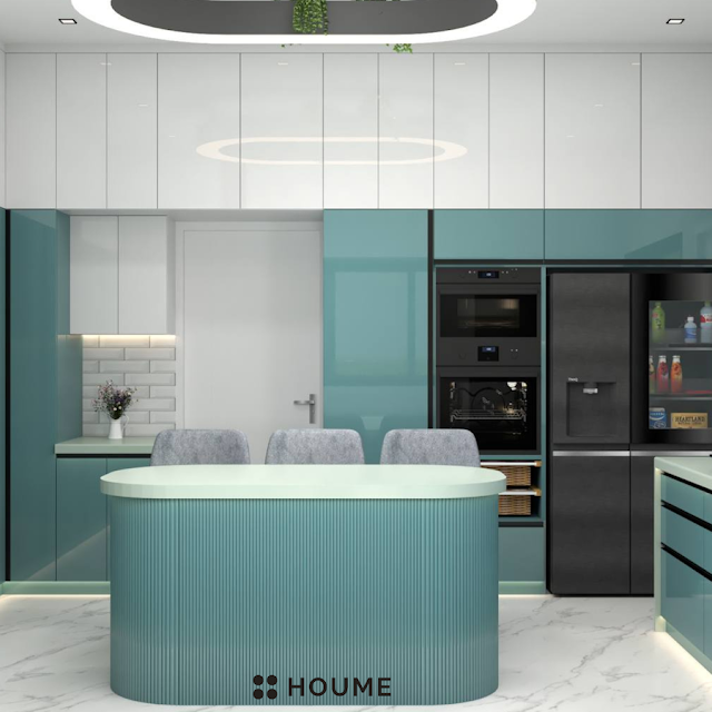 Kitchen with a stainless steel stove and a black pot simmering on the burner. A window with a black metal frame is above the stove, revealing a green backyard. A white patterned tile backsplash adds a decorative touch behind the stove. Text overlay: Houme India - Kitchen Design Ideas. B