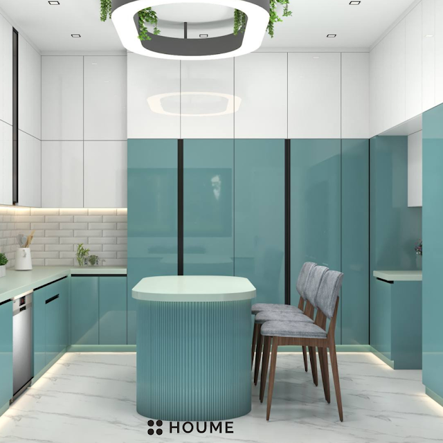 Kitchen with a stainless steel stove and a black pot simmering on the burner. A window with a black metal frame is above the stove, revealing a green backyard. A white patterned tile backsplash adds a decorative touch behind the stove. Text overlay: Houme India - Kitchen Design Ideas. C