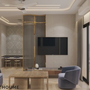 Living room featuring a large leaning mirror with a brushed gold metal frame, a round jute rug in a light natural color, and a white boucle armchair with a curved wooden frame. Text overlay: Houme India - Interior Design Ideas. B