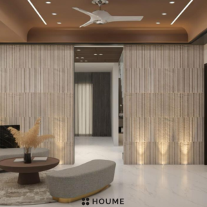 Living room featuring a large leaning mirror with a gold metal frame, a round jute rug in a light natural color, and a white boucle armchair with a wooden frame. Text overlay: Houme India - Interior Design Ideas. C