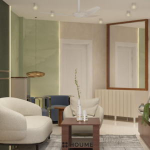Living room featuring a mid-century modern olive green fabric sofa with a tufted back and tapered wooden legs. A round wood coffee table with splayed legs sits on a cream colored area rug. Text overlay: Houme India - Interior Design Ideas. C