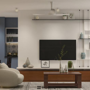 Living room featuring a mid-century modern olive green fabric sofa with a tufted back and tapered wooden legs. A round wood coffee table with splayed legs sits on a cream colored area rug. Text overlay: Houme India - Interior Design Ideas. D