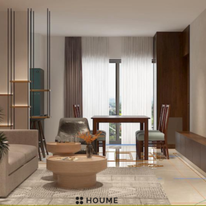 Living room with a modern gray couch, two brown accent chairs, and a round wooden coffee table with black metal legs. A woven jute rug sits underneath the furniture, and a large plant adds a touch of nature to the space. Text overlay: Houme India - Interior Design Ideas. B