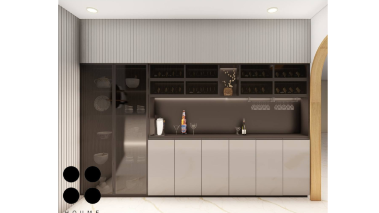 Modern kitchen interior featuring white cabinets with chrome hardware and white quartz countertops. A stainless steel sink and faucet are visible in the foreground, with a built-in oven and microwave stacked in a tall cabinet to the left and a built-in dishwasher beneath the counter to the right. Text overlay: Houme India - Interior Design Ideas. C