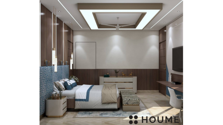 Bedroom interior featuring a king-size bed with a dark wood headboard and white bedding. A white nightstand with a lamp sits on the left side of the bed. There is a window with white blinds on the left wall. Text overlay: Houme India - Interior Design Ideas. C