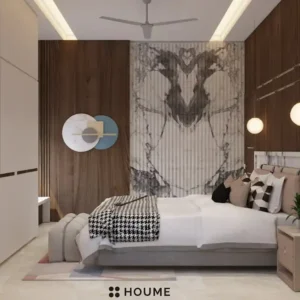 Mid-century modern bedroom interior featuring a platform bed with a walnut wood frame, a woven cream blanket and pillows, and a round wooden nightstand with a drawer. A woven jute rug covers the floor. A ceiling fan with woven blades hangs from the ceiling. The wall behind the bed is painted a light blue color. Text overlay: Houme India - Interior Design Ideas. C