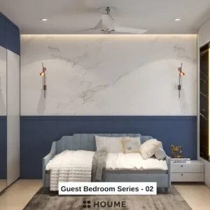 Cozy guest bedroom interior featuring a blue daybed with a white comforter and pillows. A nightstand with a lamp sits beside the daybed. A ceiling fan hangs from the ceiling. Text overlay: Houme India - Interior Design Ideas.