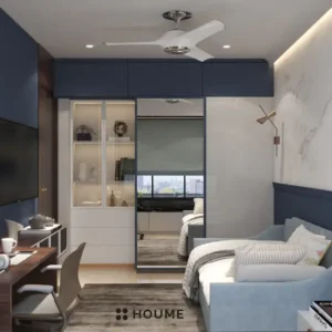 Cozy guest bedroom interior featuring a blue daybed with a white comforter and pillows. A nightstand with a lamp sits beside the daybed. A ceiling fan hangs from the ceiling. Text overlay: Houme India - Interior Design Ideas. B