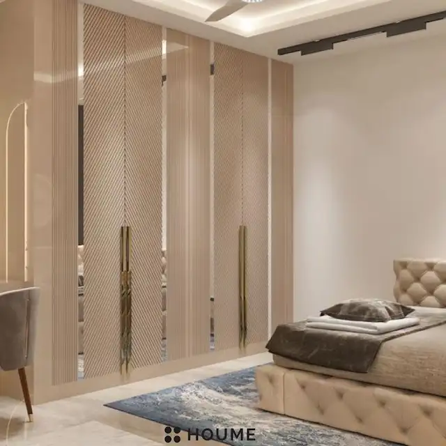 Mid-century modern bedroom interior featuring a platform bed with a walnut wood frame, a woven cream blanket and pillows, and a round wooden nightstand with a drawer. A woven jute rug covers the floor. A ceiling fan with woven blades hangs from the ceiling. Text overlay: Houme India - Interior Design Ideas. B