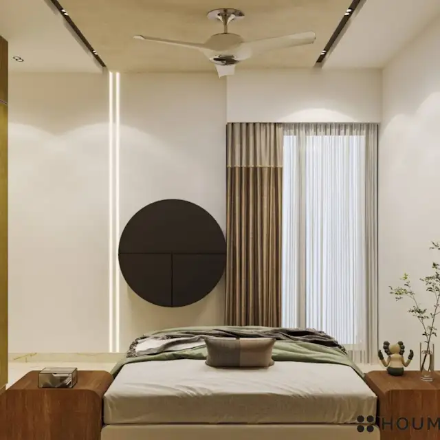 Mid-century modern bedroom interior with a low profile platform bed in walnut wood with a woven cream blanket and pillows. A round wooden nightstand with a single drawer sits beside the bed. A woven jute rug in a light natural color covers the floor. Text overlay: Houme India - Interior Design Ideas. B