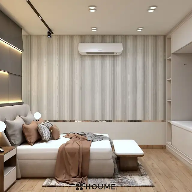 Mid-century modern bedroom featuring a platform bed with a walnut wood frame, a woven cream blanket and pillows, and a round wooden nightstand with a drawer. A woven jute rug covers the floor. A ceiling fan with woven blades hangs from the ceiling. Text overlay: Houme India - Interior Design Ideas. B