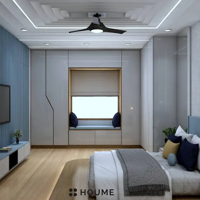 Bedroom featuring a mid-century modern bed with a tufted headboard and tapered wooden legs. A round wooden nightstand with a drawer sits beside the bed. A woven jute rug in a light natural color is on the floor. Text overlay: Houme India - Interior Design Ideas. B