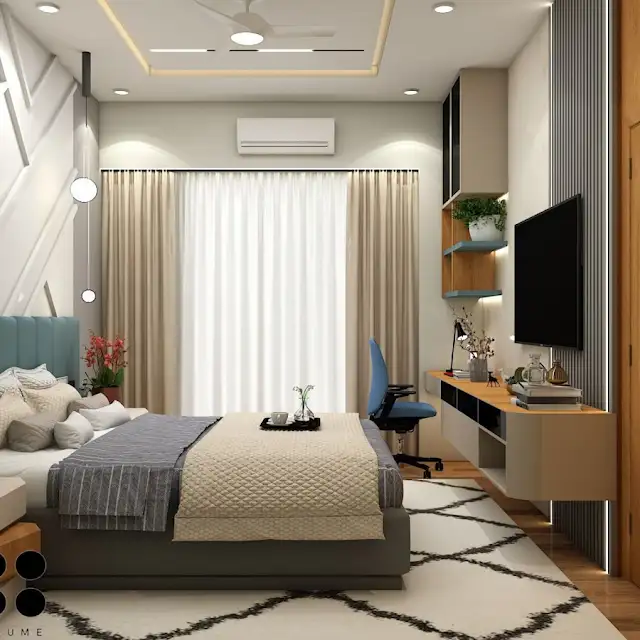 Bedroom interior featuring a wooden platform bed with a white quilt and pillows. A wooden nightstand with a woven basket sits beside the bed. A table lamp with a white shade sits on the nightstand. A woven rug in a light natural color is on the floor. Text overlay: Houme India - Interior Design Ideas. C