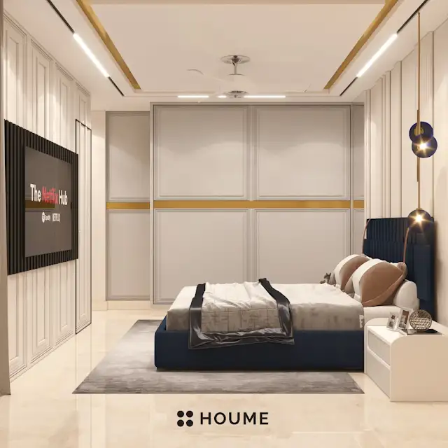 Bedroom featuring a mid-century modern platform bed with a walnut wood frame, a woven cream blanket and pillows. A round wooden nightstand with a drawer sits beside the bed. A woven jute rug in a light natural color covers the floor. A ceiling fan with woven blades hangs from the ceiling. Text overlay: Houme India - Interior Design Ideas. C