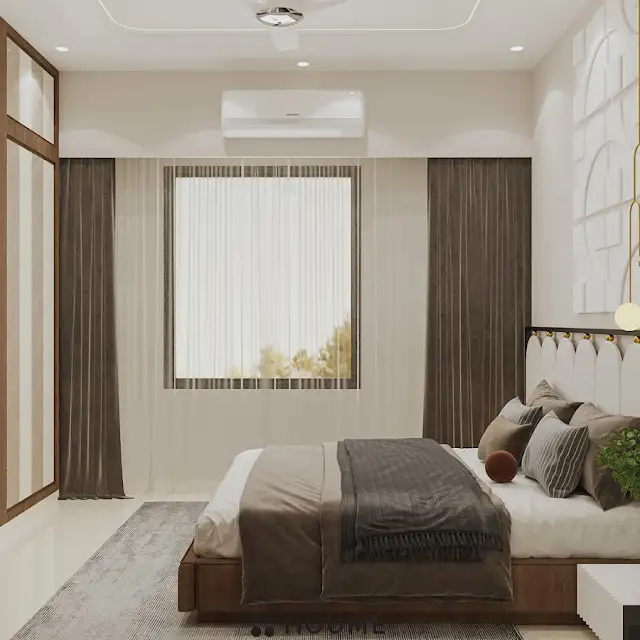 Bedroom featuring a platform bed with a textured white quilt and pillows. A wooden nightstand with a woven storage basket sits beside the bed. A table lamp with a white shade sits on the nightstand. Text overlay: Houme India - Interior Design Ideas. D