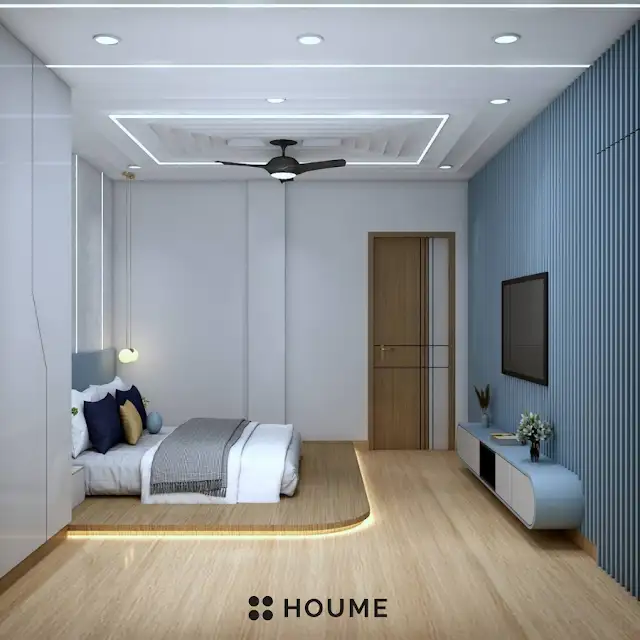 Bedroom featuring a ceiling fan with woven blades hanging from the ceiling. A brown leather couch sits on a woven jute rug in the center of the room. Two brown accent chairs with nailhead trim flank a round wooden coffee table with a black metal base. Text overlay: Houme India - Interior Design Ideas. D
