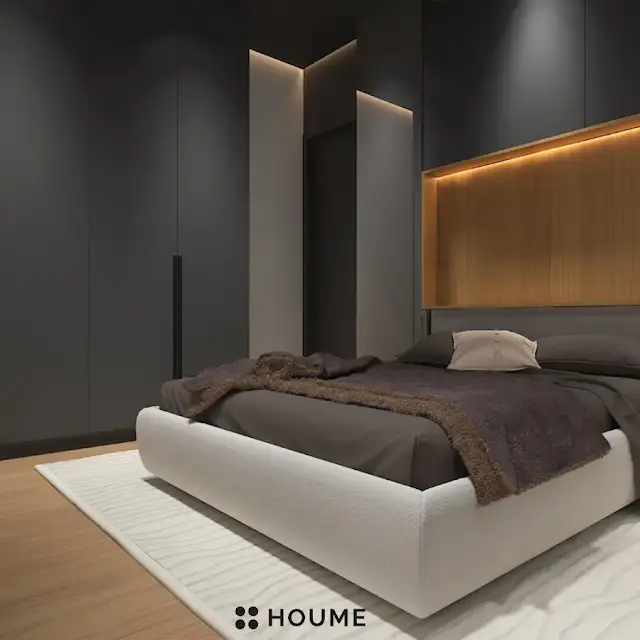 Mid-century modern master bedroom interior featuring a low profile platform bed in walnut wood with a woven cream blanket and pillows. A round wooden nightstand with a drawer sits beside the bed. A woven jute rug in a light natural color covers the floor. A ceiling fan with woven blades hangs from the ceiling. Text overlay: Houme India - Interior Design Ideas. B