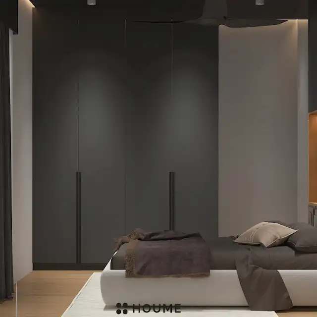 Mid-century modern master bedroom interior featuring a low profile platform bed in walnut wood with a woven cream blanket and pillows. A round wooden nightstand with a drawer sits beside the bed. A woven jute rug in a light natural color covers the floor. A ceiling fan with woven blades hangs from the ceiling. Text overlay: Houme India - Interior Design Ideas. D