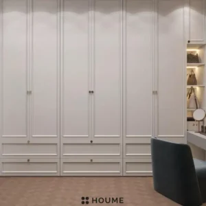 Walk-in closet interior featuring a vanity with a white countertop, a rectangular mirror with a chrome frame above the countertop, and open wood shelves lining the walls. Text overlay: Houme India - Interior Design Ideas. C