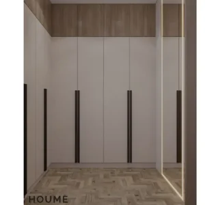 Mid-century modern bedroom interior featuring a platform bed with a walnut wood frame, a woven cream blanket and pillows, and a round wooden nightstand with a drawer. A woven jute rug covers the floor. A ceiling fan with woven blades hangs from the ceiling. The wall behind the bed is painted a light blue color. Text overlay: Houme India - Interior Design Ideas. B