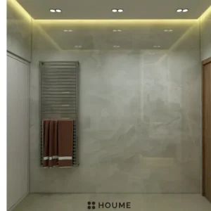 Simple, clean bathroom interior featuring a white toilet, pedestal sink with a chrome faucet, and a rectangular mirror with a chrome frame above the sink. The walls are a light beige color and there is a window with frosted glass on the right wall. Text overlay: Houme India - Interior Design Ideas. B