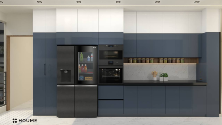 A photorealistic rendering of a modern kitchen design by Houme India. The kitchen features blue-grey and white cabinets with black accents, a sleek countertop, and glass cabinet doors with ribbed glass inserts. B