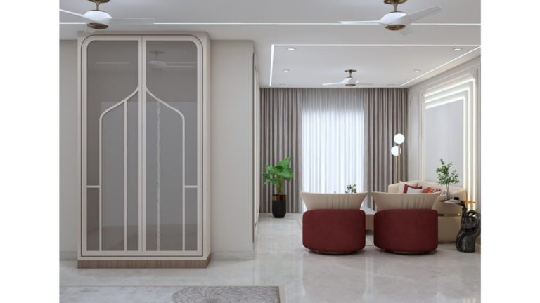 A modern Indian living room with a beige sofa, red accent chairs, a geometric rug, and a decorative wall panel. E