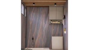 A modern washroom design by Houme India with a gray textured accent wall, black bathroom fixtures, and a wooden ceiling with recessed lighting. C