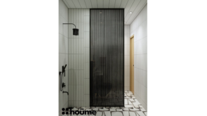 A modern washroom by Houme India with green tiles on one wall, a textured stone floor, a wooden accent wall, and a glass enclosed shower. B