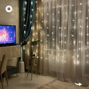 A living room with sheer curtains adorned with warm-white fairy lights, creating a cozy ambiance.