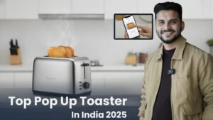 A close-up of a modern, silver and black pop-up toaster on a clean kitchen counter, actively toasting bread. A man (Sourabh) in a professional beige jacket gestures toward the appliance. An inset image highlights a control panel or dial. The bold title, "Top Pop-Up Toaster In India 2025" is visible at the bottom.